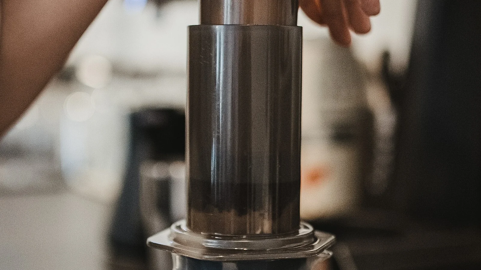 A person pressing an AeroPress over a glass coffee server