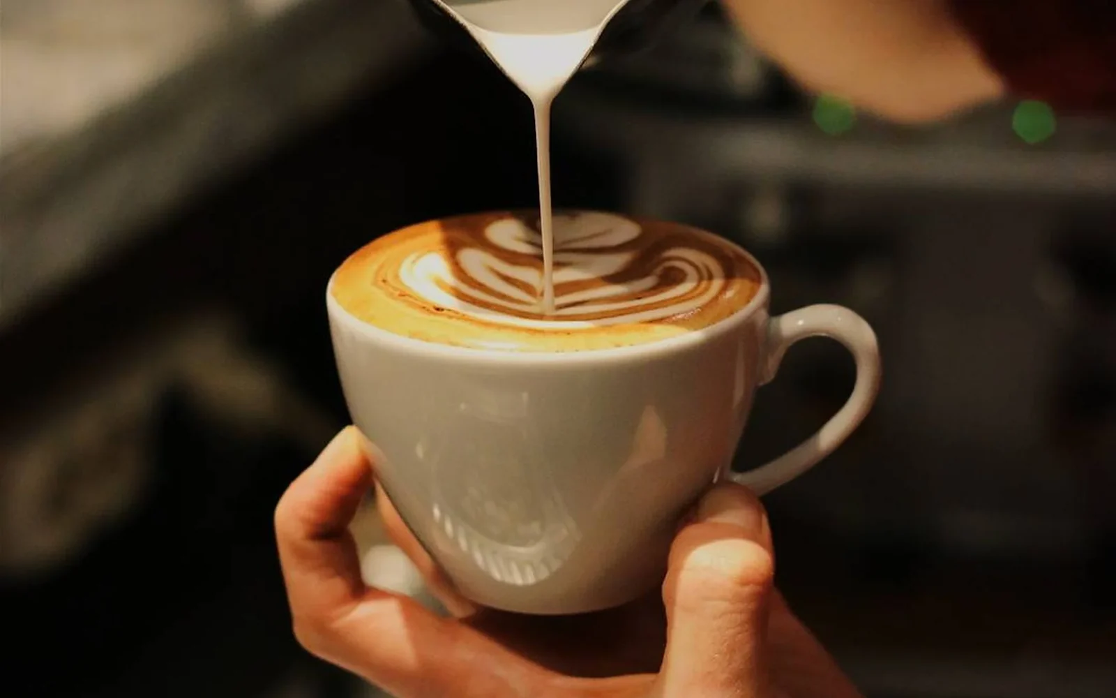 Barista pouring thin glossy microfoam into a small coffee cup