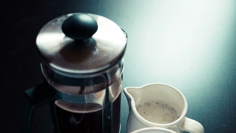 French press beside a white coffee cup on a table