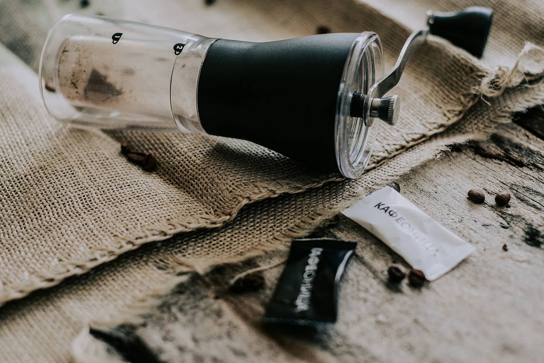 Hand coffee grinder on burlap beside coffee beans