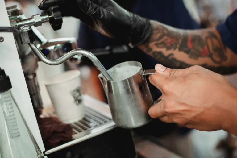 Barista steaming milk in a steel pitcher using an espresso-machine wand