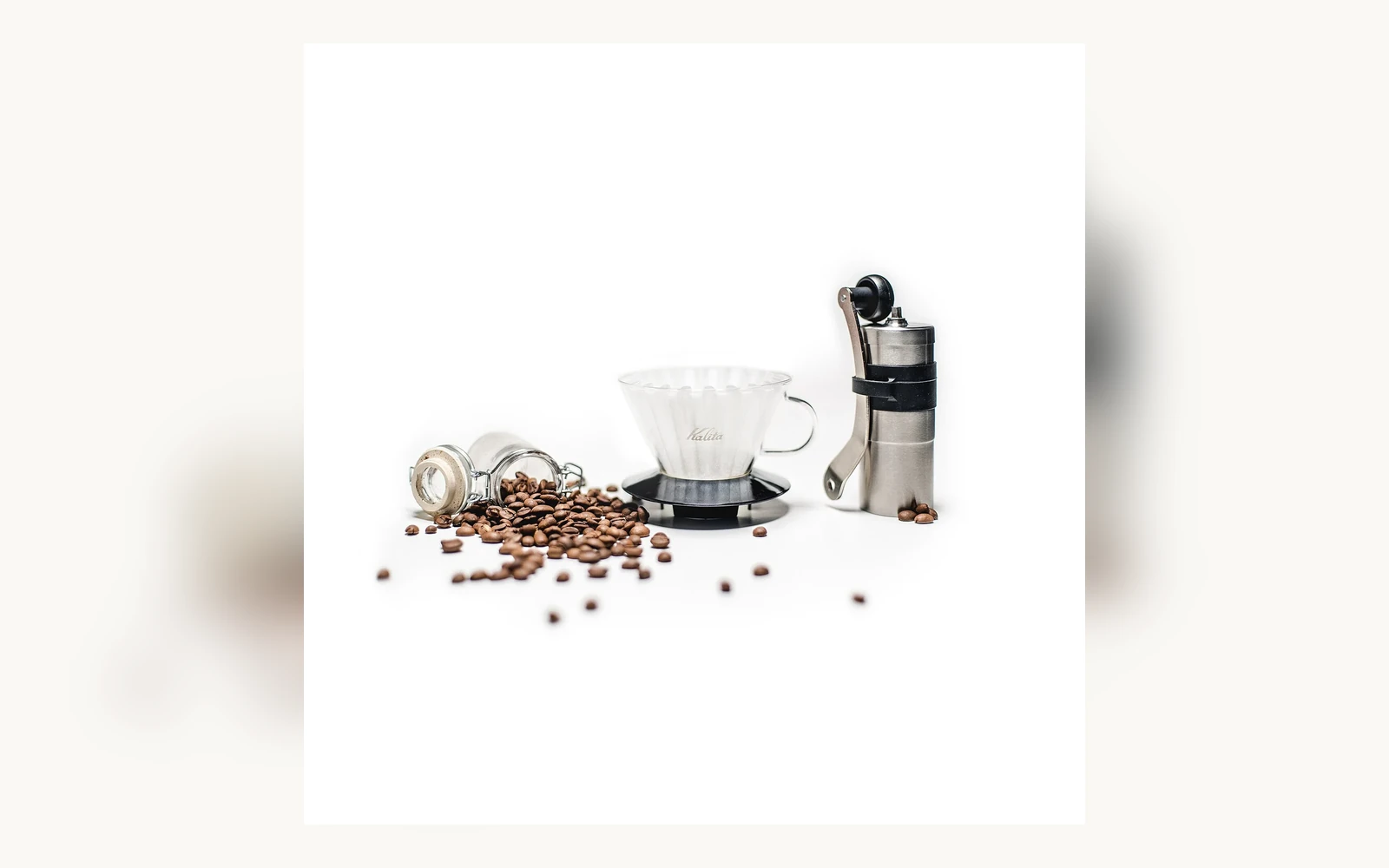Whole coffee beans beside a hand grinder and pour-over brewer