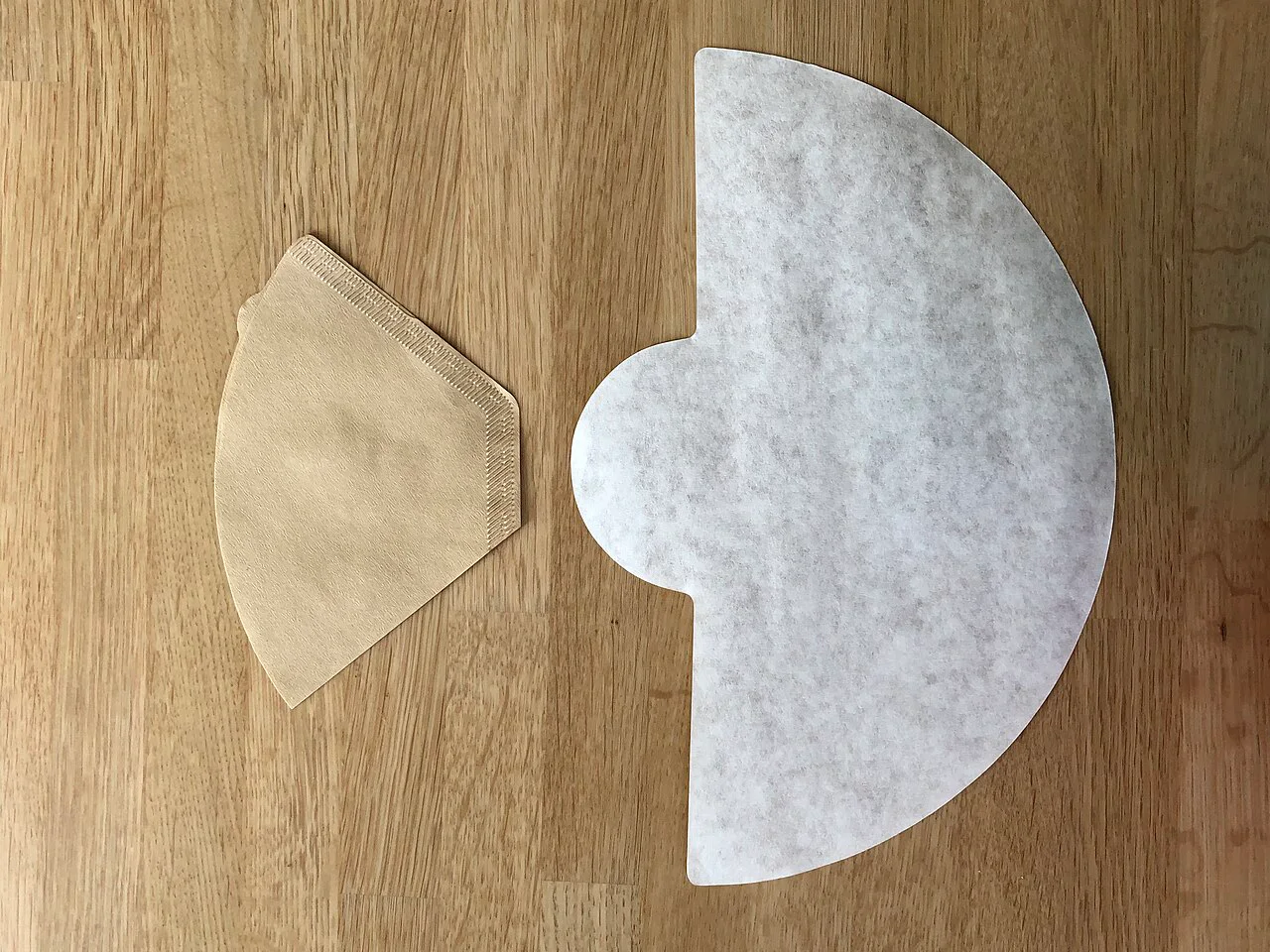 A brown cone paper beside an unfolded white Chemex half-moon filter