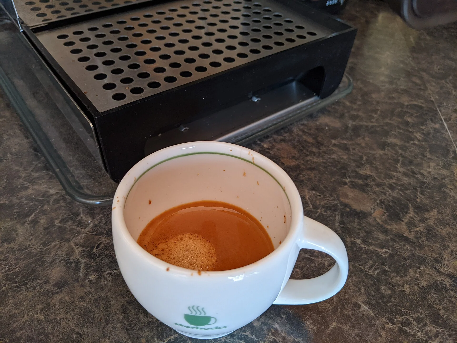 Espresso in a white cappuccino cup beside a home coffee machine