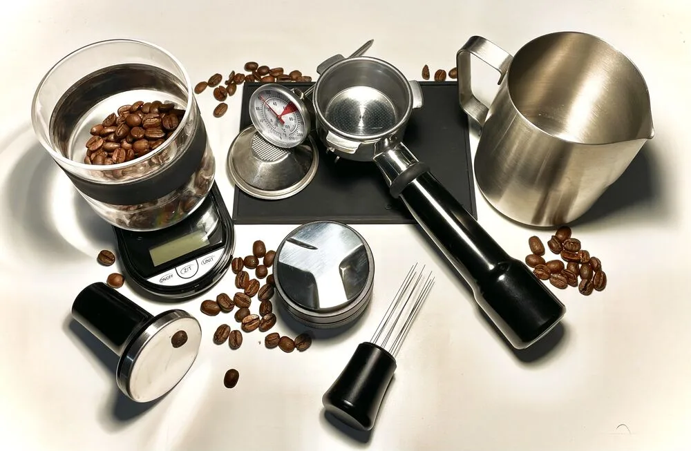 Milk thermometer beside a stainless steel milk pitcher and espresso tools